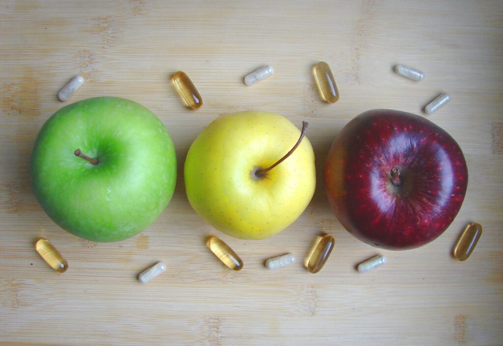 Three apples, green, yellow and red. Pills are aroung them